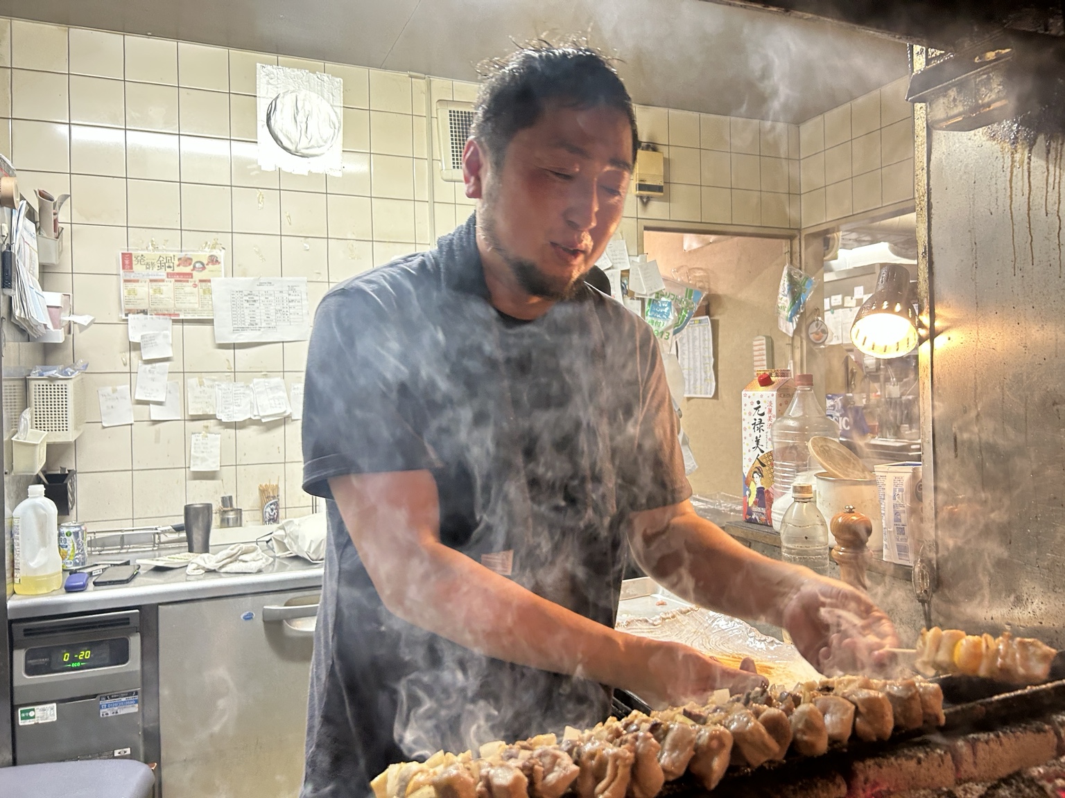 福よし岩見沢店で串を焼くマスター。立ちのぼる煙の中、焼き台に向き合う姿。